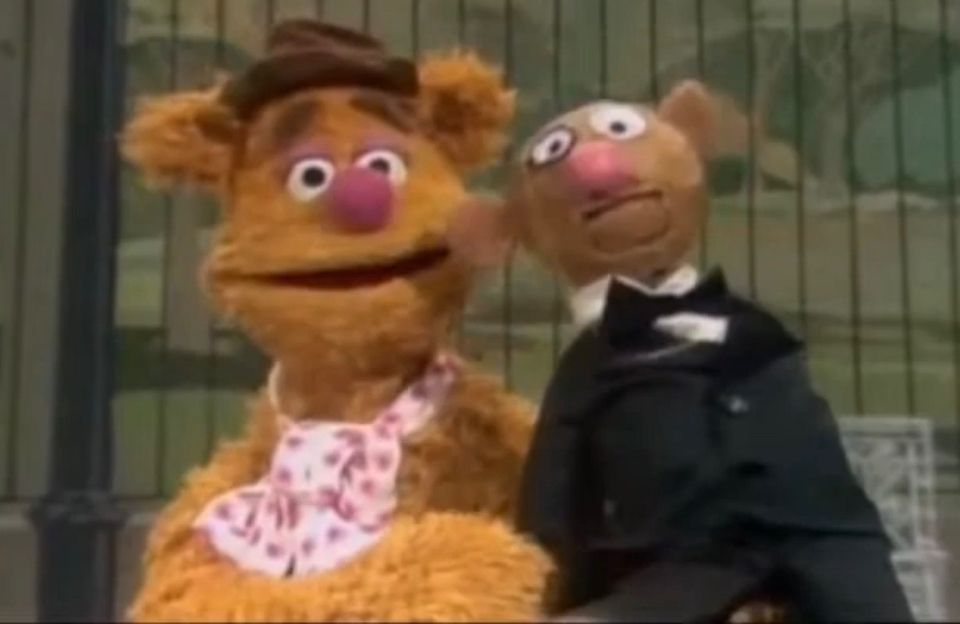Fozzie Bear holding a ventriloquist dummy of himself with a monocle and a tuxedo