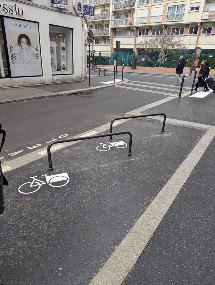 A cargo bike bay surrounded by a kerb. There is a crossing point for pedestrians beyond it marked in white with tactile paving. 