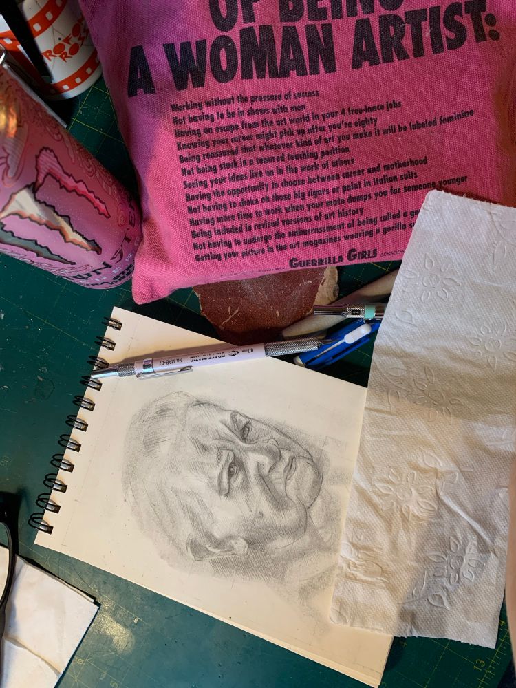 Översikt en arbetsbänk. I fokus en skiss av en äldre kvinna. Pennor är strödda runt, ett Guerrilla girls pennskrin och en energidricka