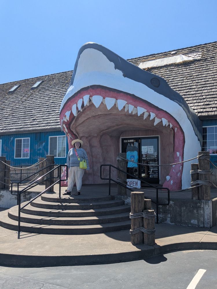 Woman standing at the doorway of a gift shop, which looks like a huge shark mouth 