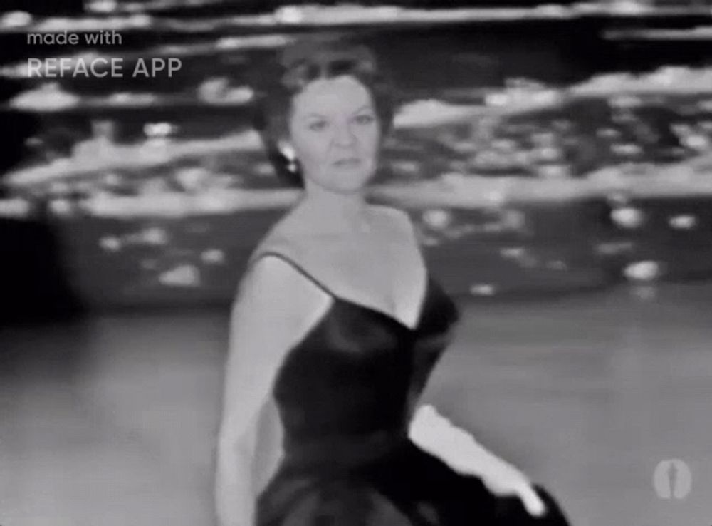 a woman in a black dress and white gloves is sitting on a stage .