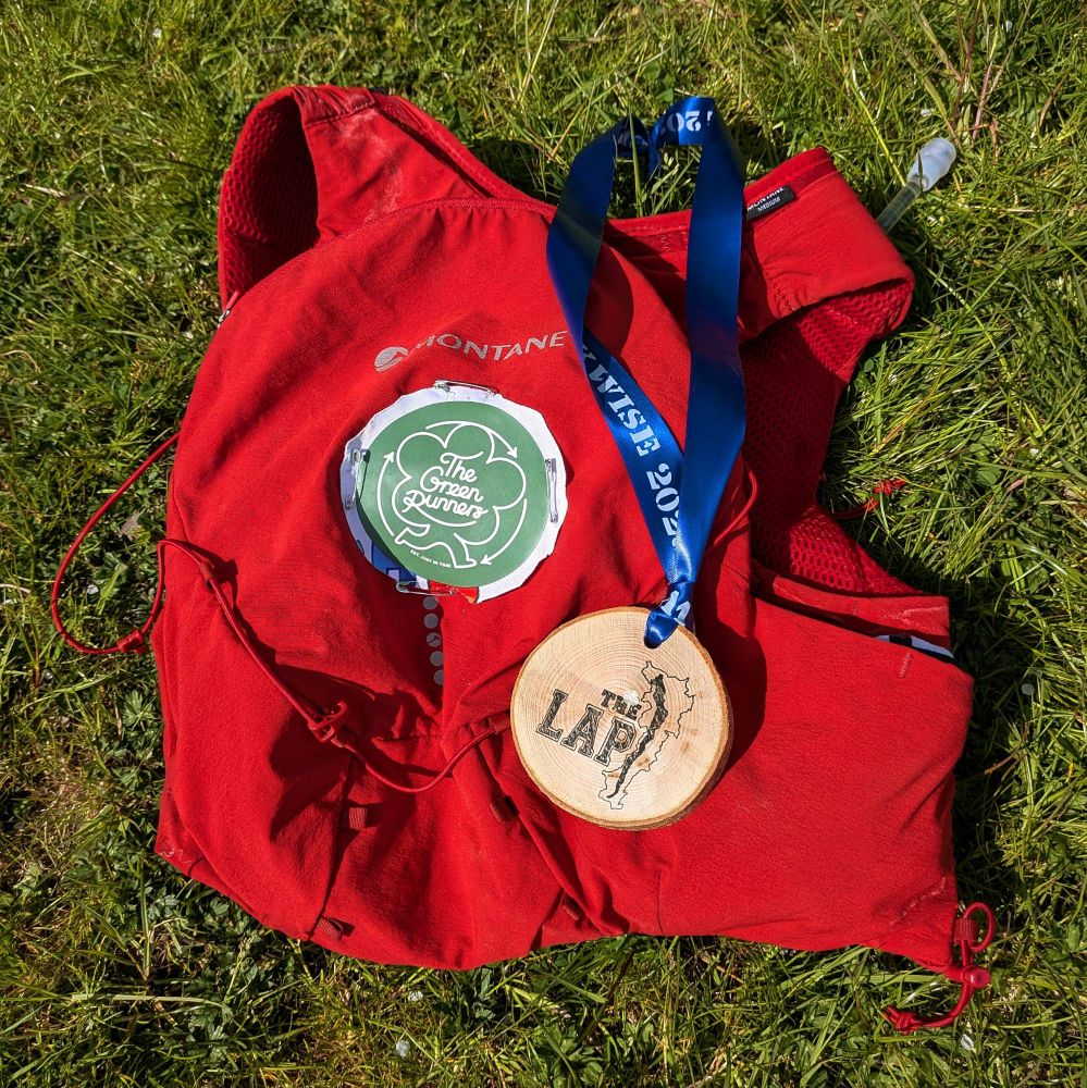 A red running backpack with a Green Runners badge safety pinned to the back and a medal from the Lap resting on top.