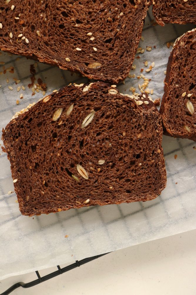 a slice of dark, chocolate-coloured bread with a roofed top, webby and dotted with seeds