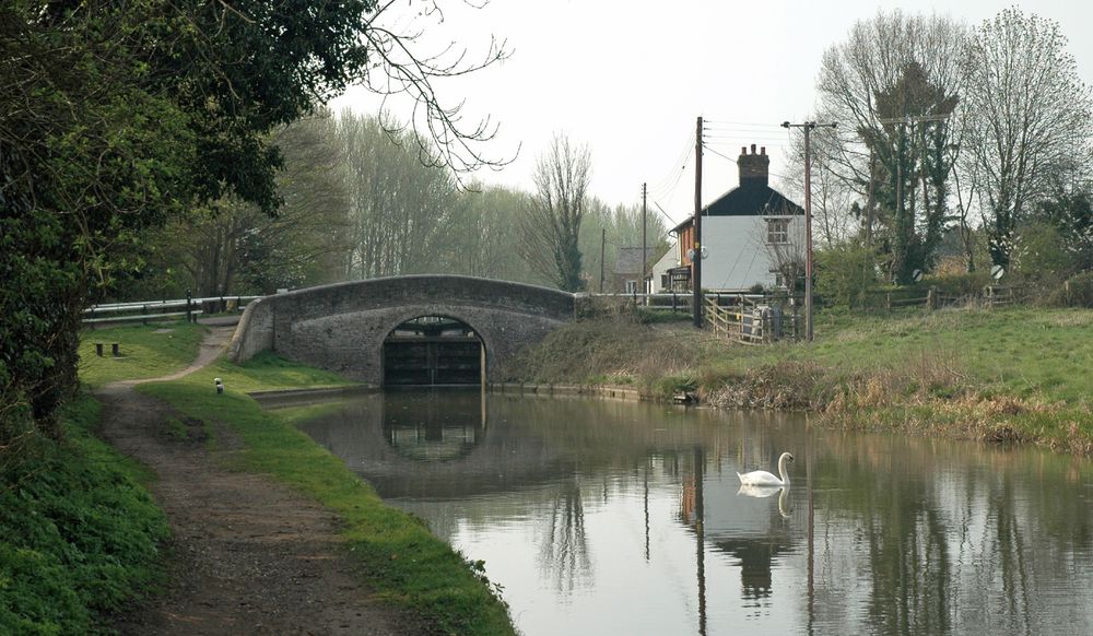 Looking back from below Dudswell lower lock on the Grand Union Canal. A swan glides on the canal. The lock gates are visible through the arch of the bridge, which acts as a roving bridge for the towpath.