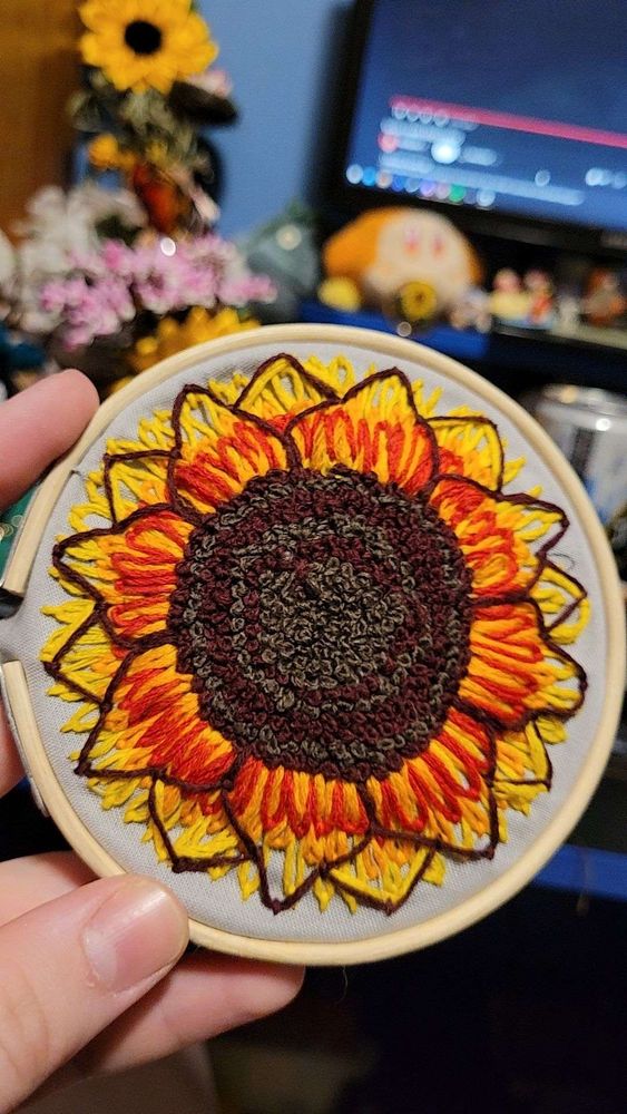 a palm-size embroidered sunflower. the petals are red-orange toward the center and yellow at the tips. the middle of the flower is brown and grey in alternating rings.