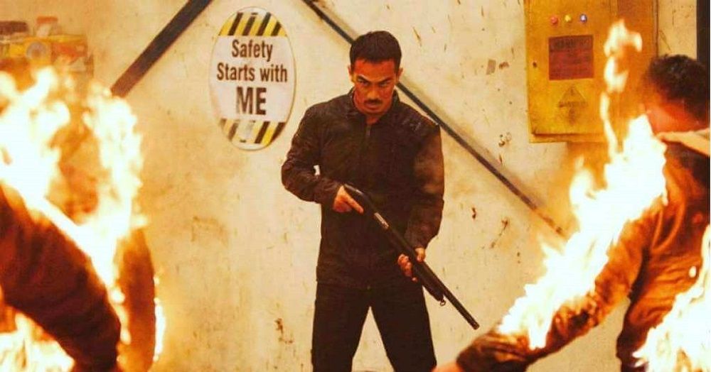 Man holding a shotgun in front of a sign that says "safety starts with ME" while people are on fire nearby