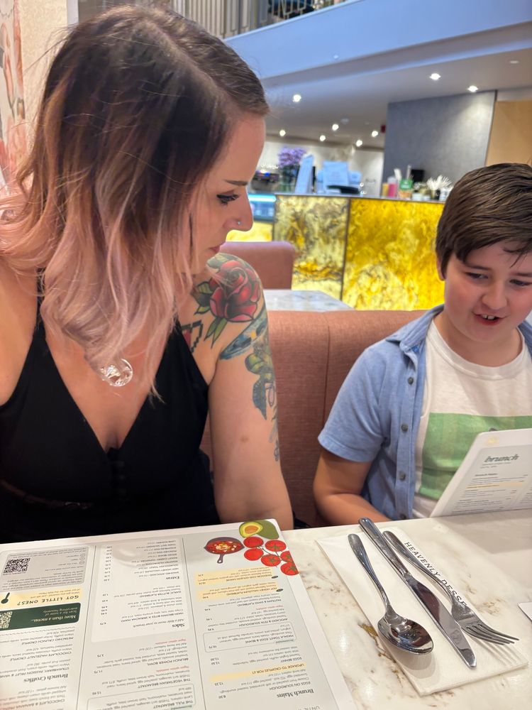 Woman with pink hair and tattoos and a young boy with a blue shirt on holding a menu