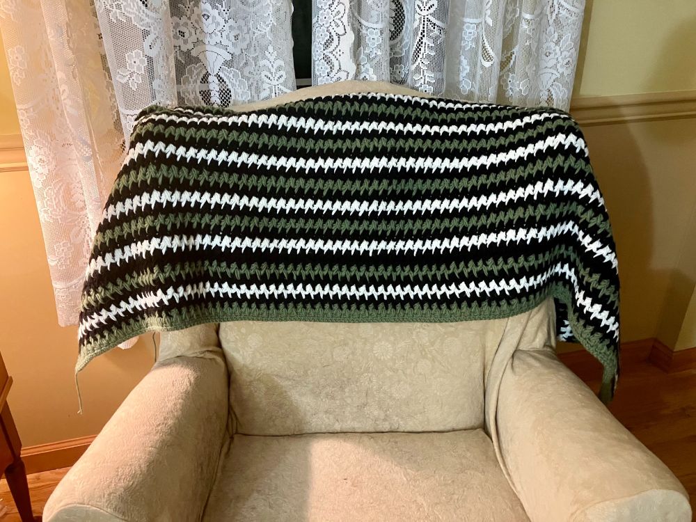 A striped blanket of black, white, and sage green drapes over the back of an ivory chair.