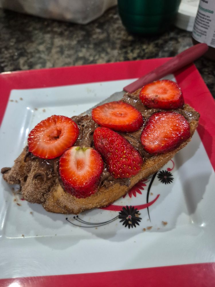 Foto de uma rabanada (pão molhado em una mistura de leite, leite condensado e açúcar, frito em óleo) com nutella e morangos por cima
