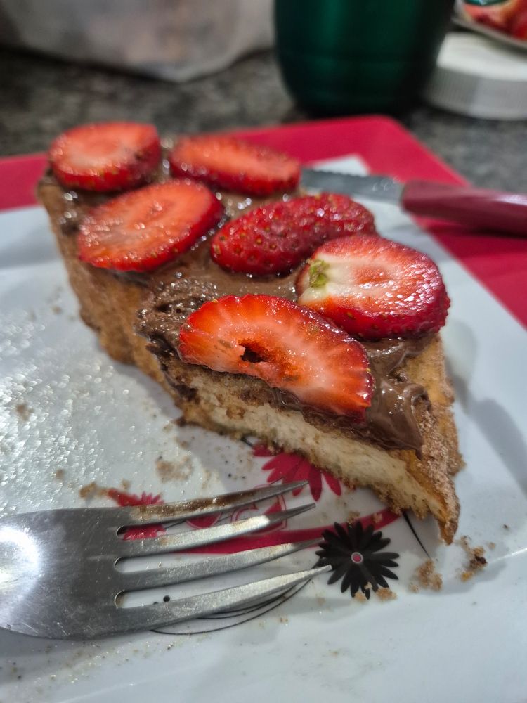 Foto de uma rabanada (pão molhado em una mistura de leite, leite condensado e açúcar, frito em óleo) com nutella e morangos por cima.