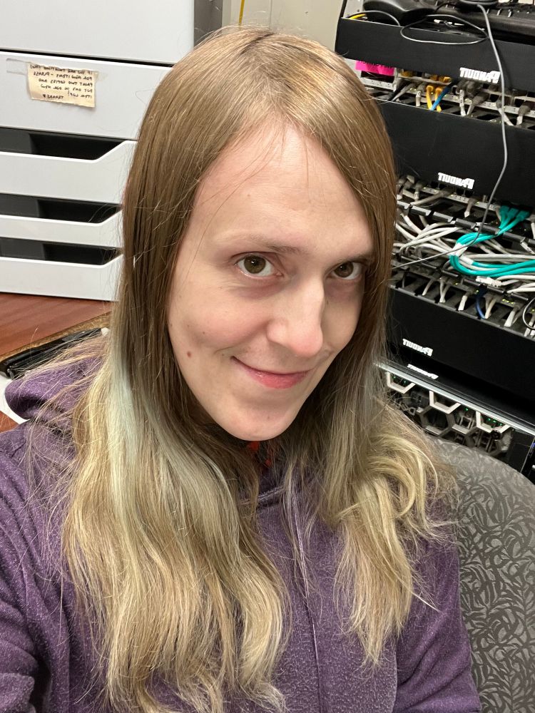 a photo of amber sitting in its office at work. it’s wearing a purple hoodie and smiling at you!