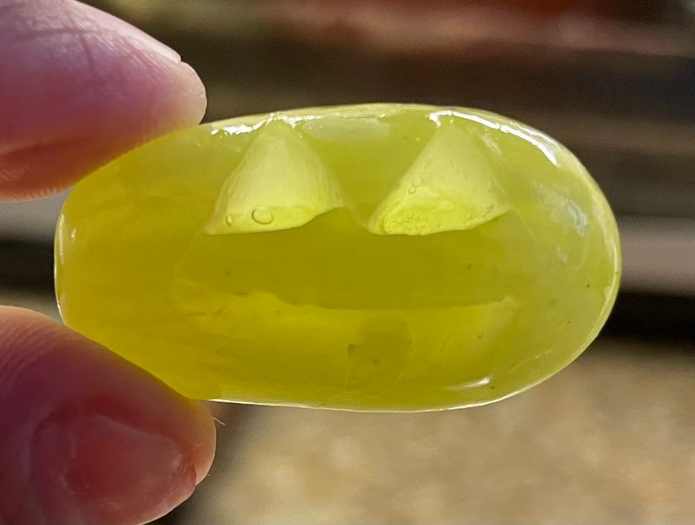 Close up photo of the author holding a green elongated grape carved as a jack-o-lantern