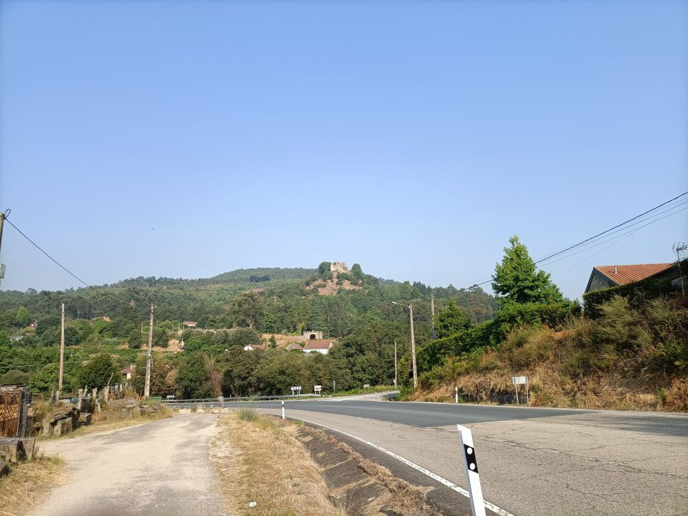 Estrada nacional e no fondo unha elevación cun castelo no alto. É o castelo de Vilasobroso, no concello de Mondariz.