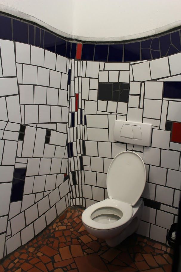 Toilette mit geöffnetem Deckel in Weiß. 
Rechteckige Fliesen in Schwarz und Weiß, krumm an den Wänden angebracht