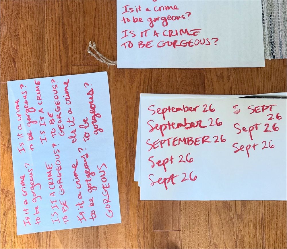Three large sheets of paper on the ground, with variations of copy written on it in lipstick.