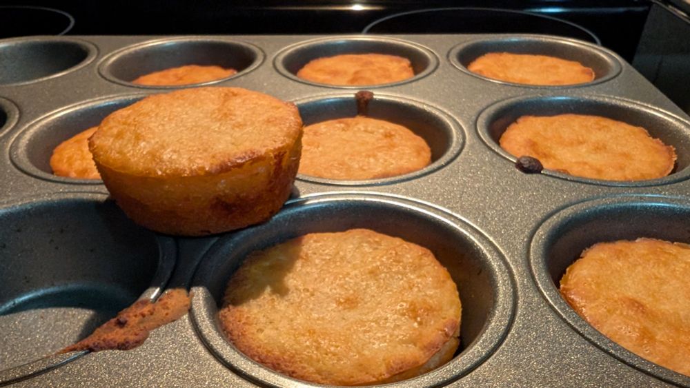 A photo of a muffin pan filled with golden brown buns. 