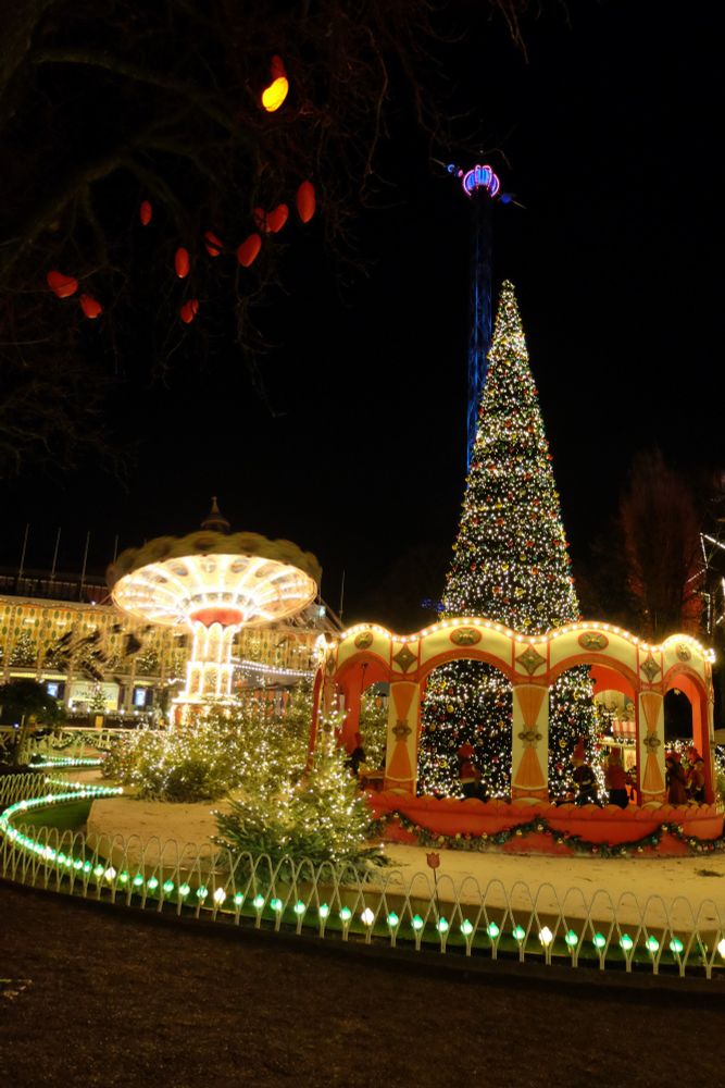 A brightly lit Christmas tree and fairground rides at night