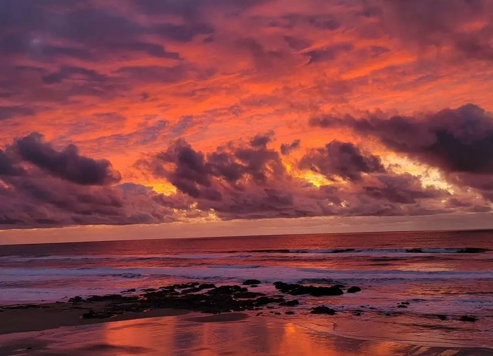 Pink, lavender and orange sunset in the clouds on a beach with a rocky area in the center