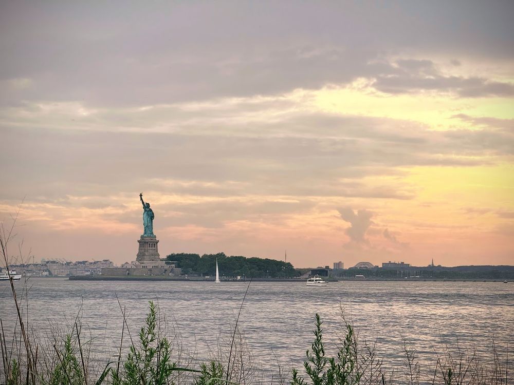 A photo of the statue of liberty at dusk. It's peaceful, and there are several small boats in the water.