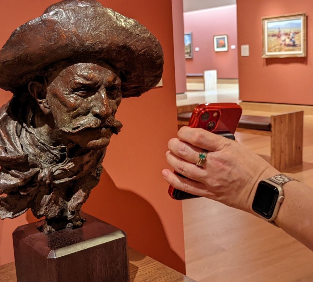 A statue’s head leaning in to look at a phone screen.