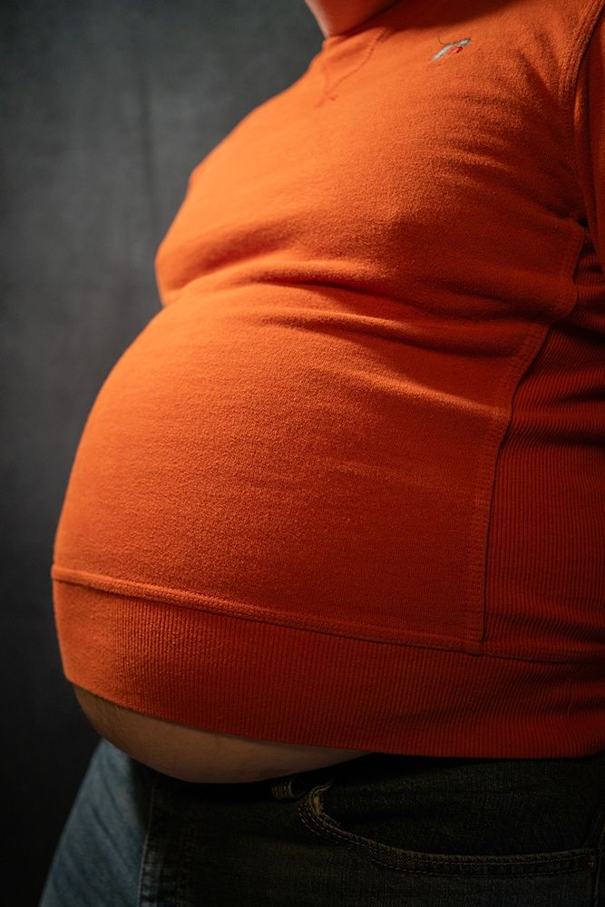 Babyblueboxers standing with an orange sweater and jeans, belly is hanging out below the shirt.