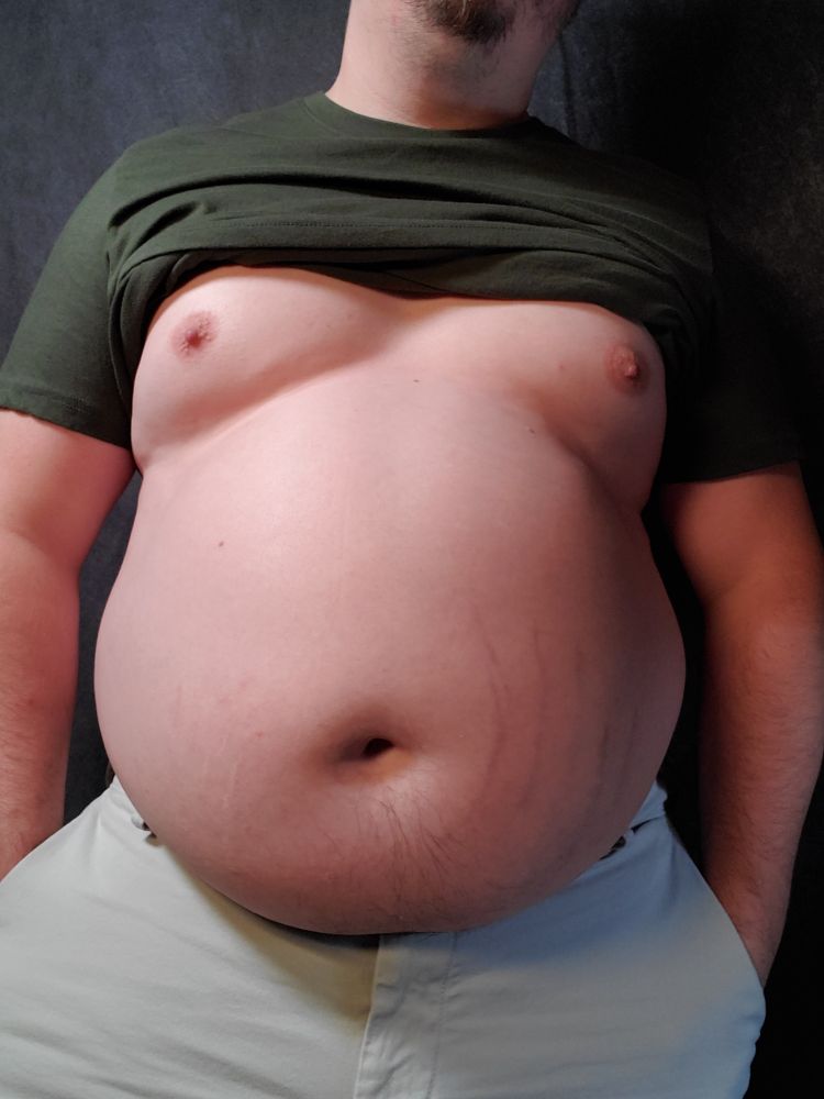 Babyblueboxers standing in a green shirt and khaki shorts. Shirt is pulled up and belly is round. 