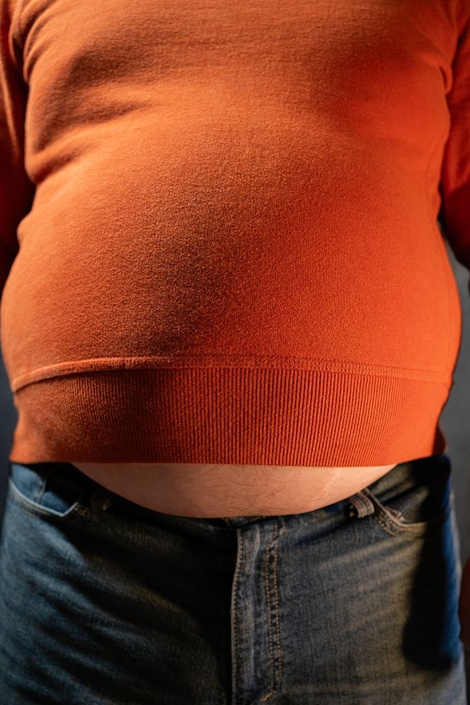 Babyblueboxersis standing, facing the camera orange sweater and jeans, belly is hanging out below the shirt.