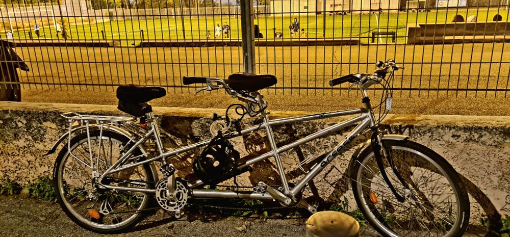 Vélo tandem accroché aux grilles d'un stade de football qui se trouve en arrière plan