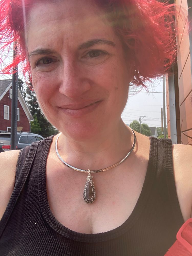 Me smiling in sunny Rockland, Maine, wearing a black tank top and a silver torque necklace with a wire-wrapped red labradorite pendant 
