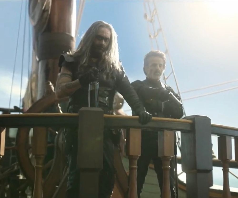 Ed and Izzy standing next to each other behind a wooden railing in the Season 1 Episode 10 of Our Flag Means Death.