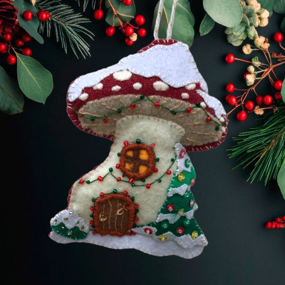 A felt ornament in the shape of a mushroom house in the middle of winter, with its own "lights" and decorated tree, plus snow on the roof.