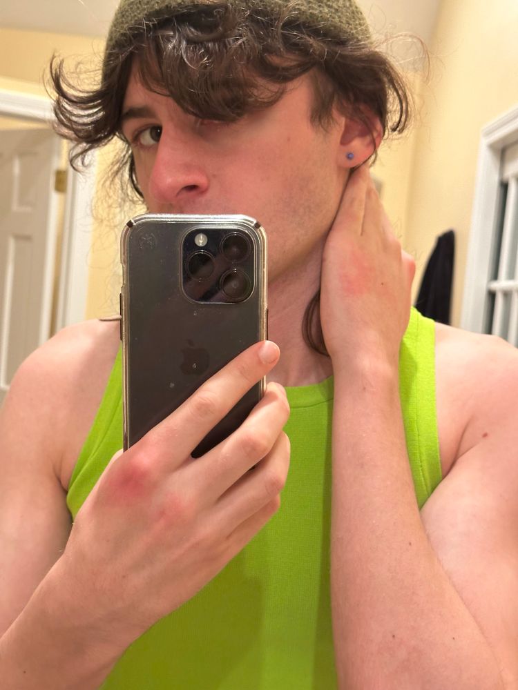 stupid twink once again wearing green perchance with a more femboy look again with purple piercings in his ears