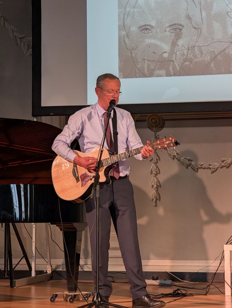 Foto von Helmut Staubmann auf der Bühne im Kaiser-Leopold-Saal mit Gitarre und Standmikrofon