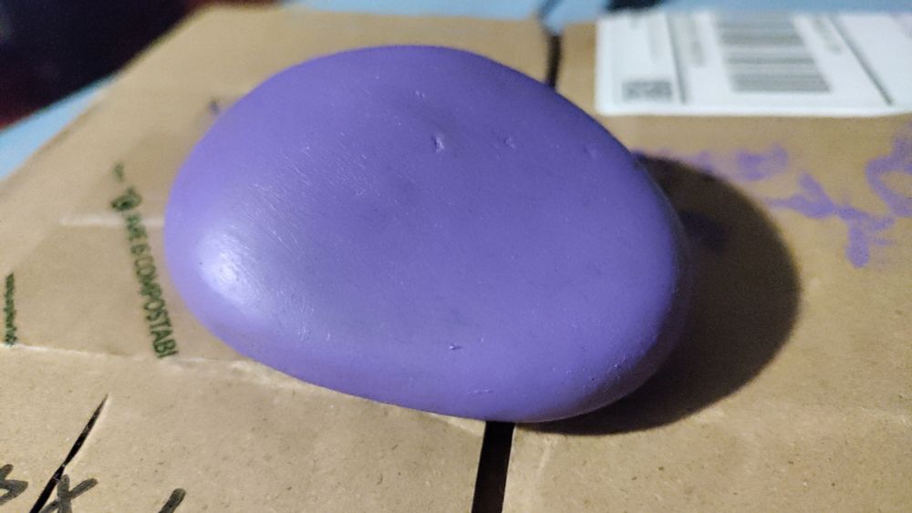 A rock painted purple, by me, on a piece of cardboard