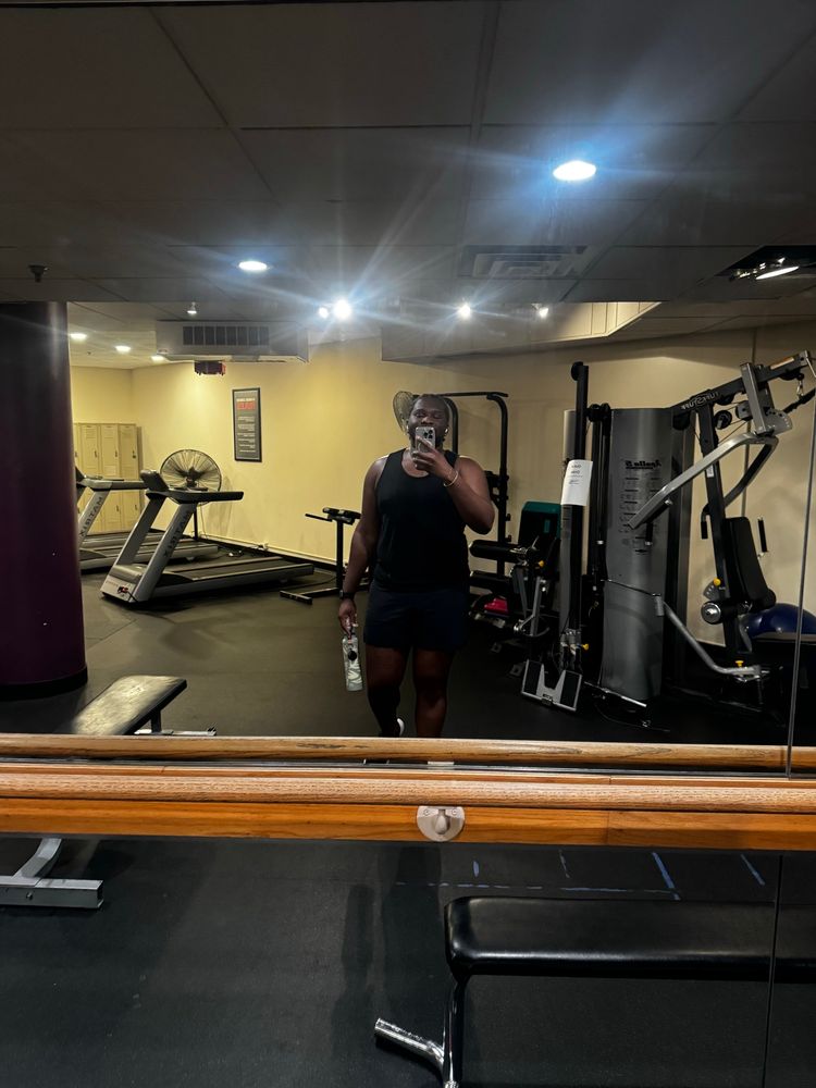 A photo of myself in a black tank top, black running shorts, holding my green water bottle in the gym