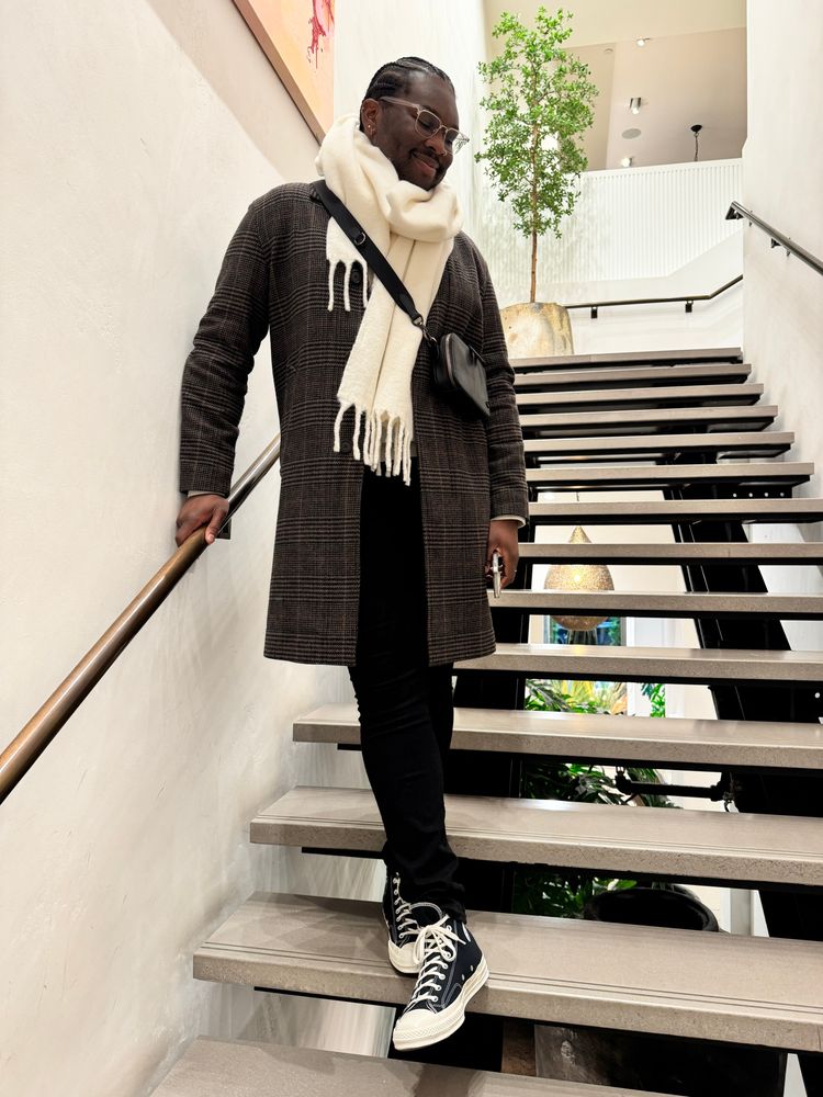 A photo of myself wearing a white scarf, brown coat, and black/white converse while standing on stairs