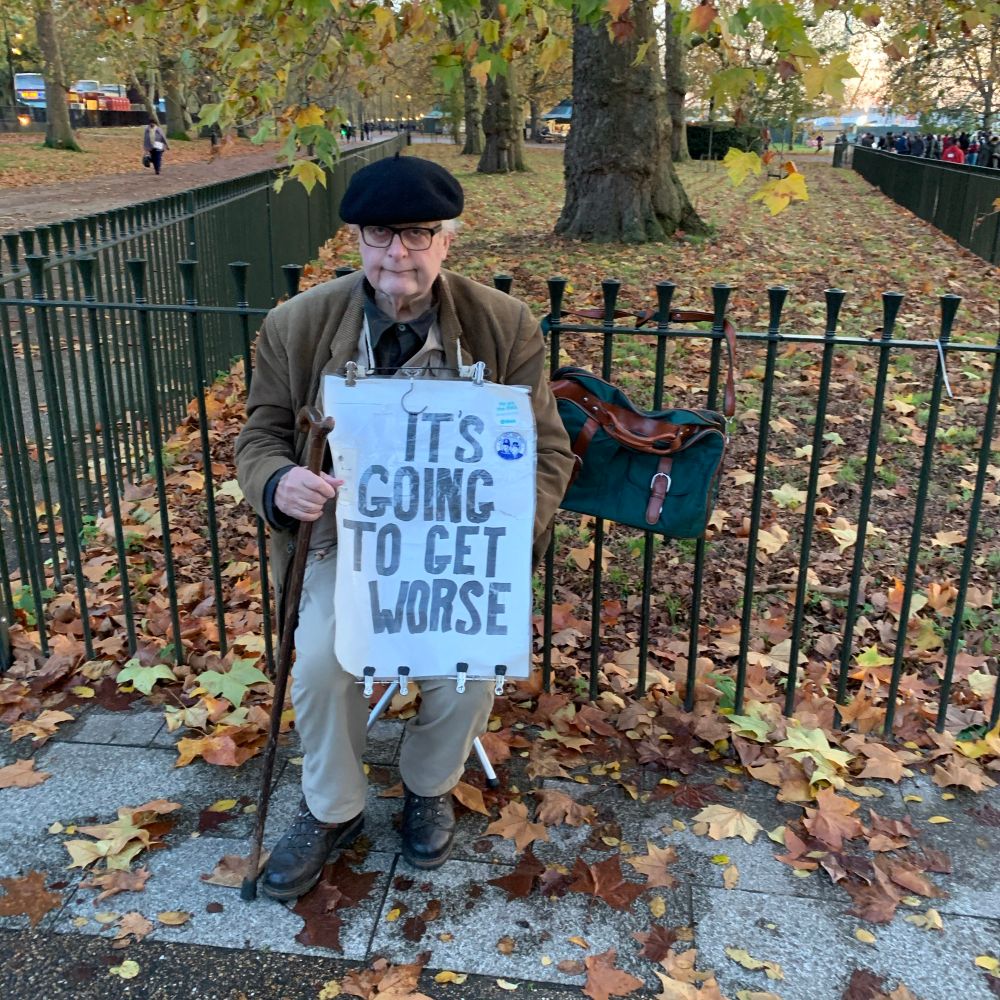 Old man holding a sign that says, “it’s going to get worse.”