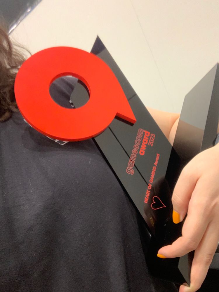Man sieht den gamescom „Heart of Gaming“ Award im Detail, wie er in einem Arm gehalten wird.
