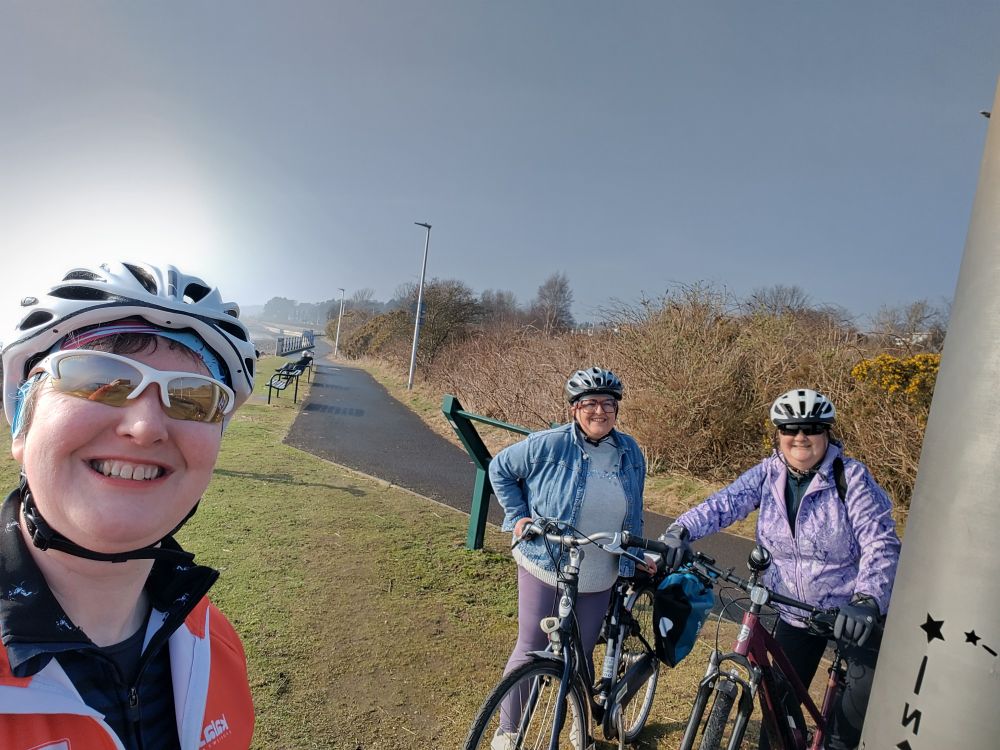 3 women smiling in the sunshine next to a traffic free path