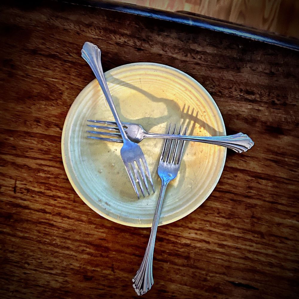 A yellow desert plate with three forks resting on it in a disturbing triangular pattern. Is this a trap for Central European demons?