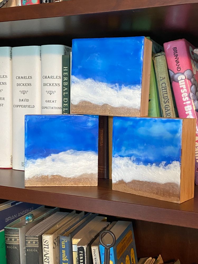 Small square abstract encaustic paintings of ocean waves with brown sandpaper beaches. 