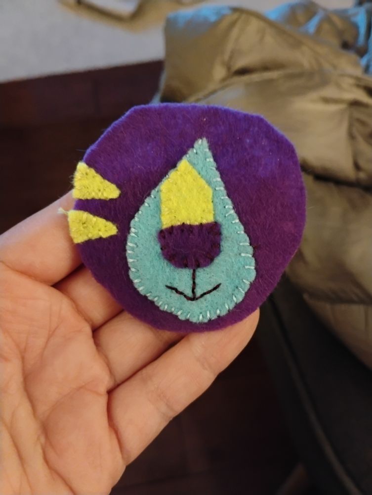 in my hand, a half finished tiger face out of neon colours. a purple face and nose, with a yellow and blue snout and yellow stripes. 