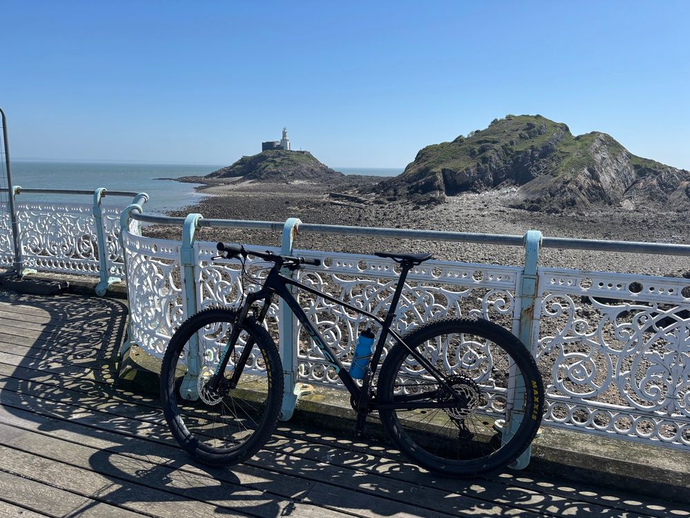 Picture of a bike leaning up against Mumbles pier railings, with Mumbles lighthouse in the background 