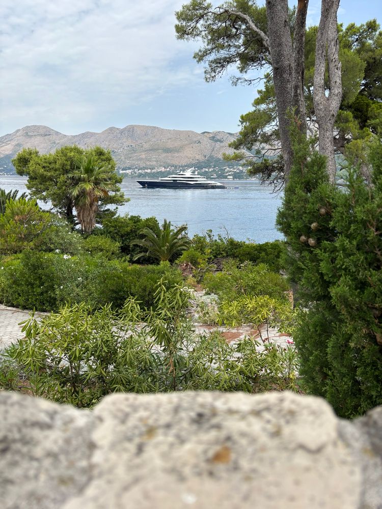 View of a yacht through tress and well kept gardens in Cavtat bay, Croatia. 