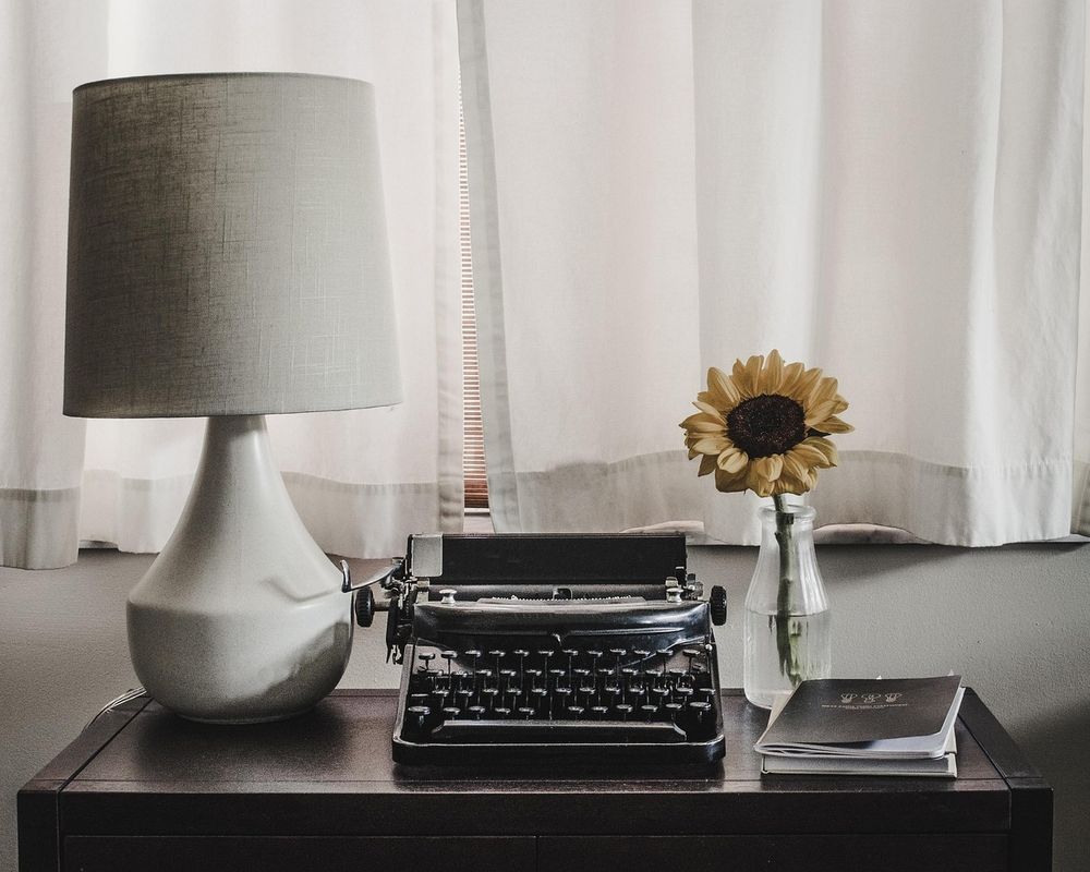 Table with a lamp, typewriter, book, and a sunflower.

Source:
Desk Typewriter Office - Free photo on Pixabay https://share.google/vqETLi5nm4Ub85EAf
