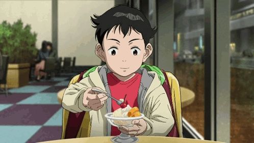 a young boy in a red shirt is eating ice cream with a cherry on top