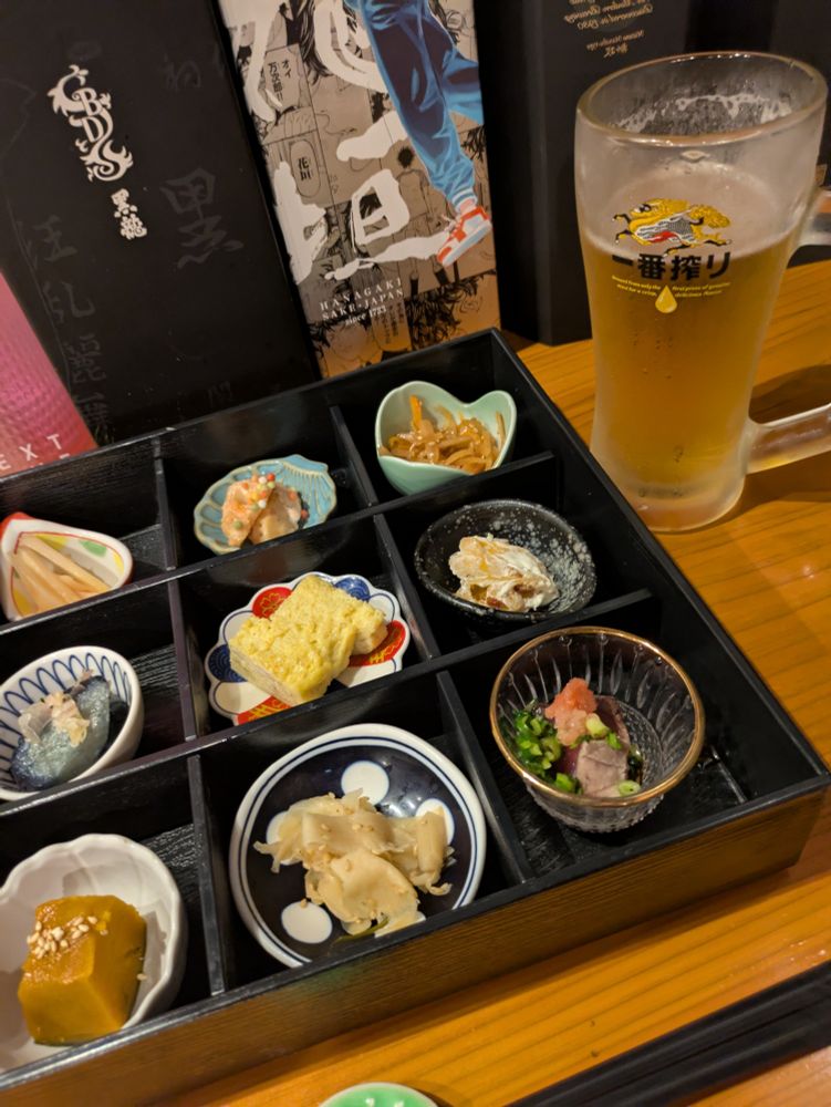 お酒のあてぎ少しずつ収まった九分割のお重に一番搾りの中ジョッキ（飲みかけ）