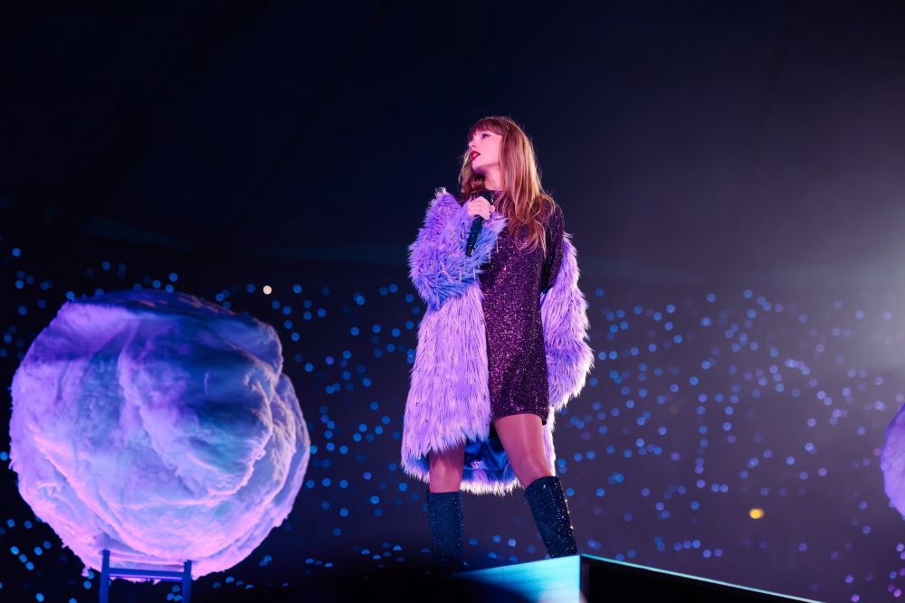 Taylor Swift performing Lavender Haze during the Midnights era of The Eras Tour. She is wearing the lavender fur coat and dark purple tshirt dress. 