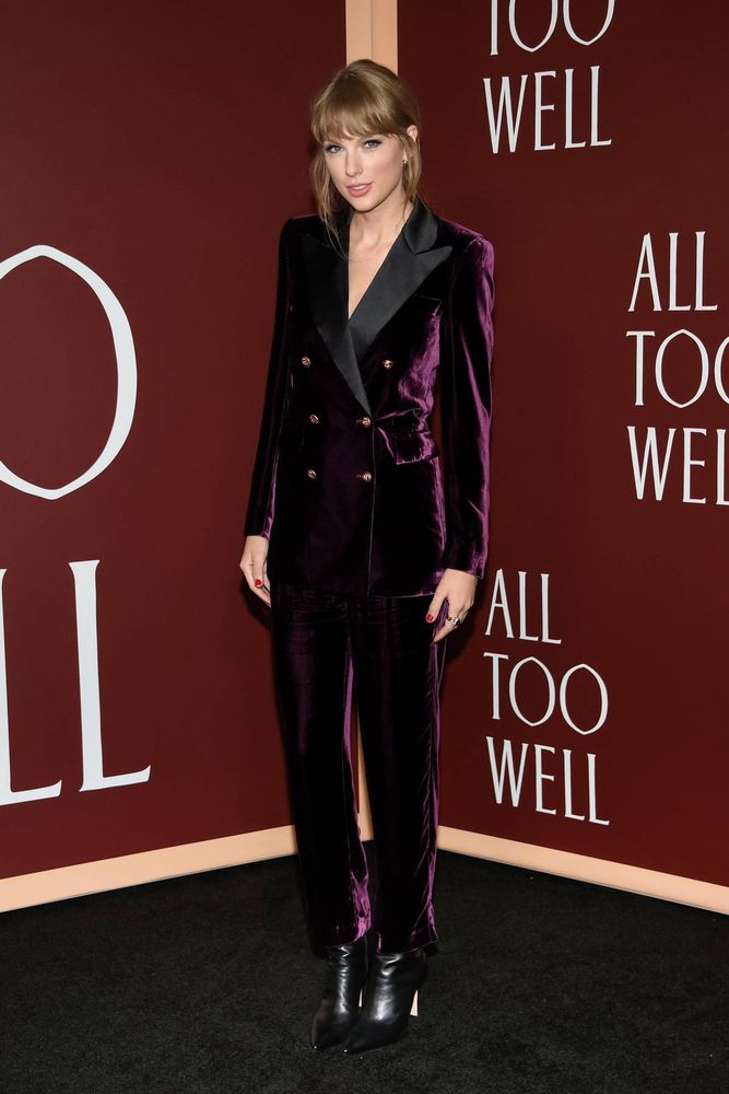 Red TV era Taylor Swift. She is at her All Too Well The Short Film premiere. She is in a purple velvet suit with black boots. She’s wearing neutral makeup with her hair in an updo. She has her nails painted red. 