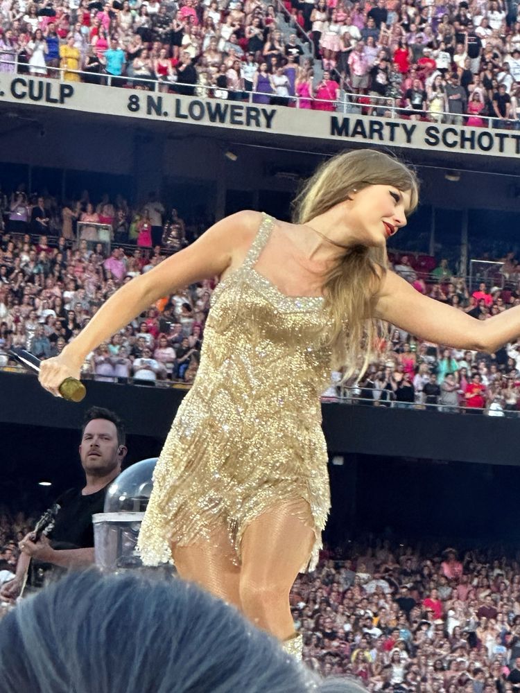Taylor Swift on stage at the eras tour during the fearless set. She’s wearing the short gold fringe dress. 